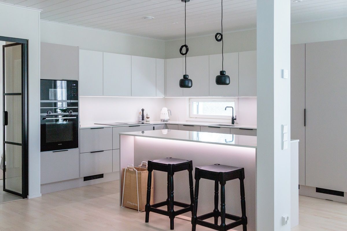 La cucina è illuminata da strip LED a tutta lunghezza in un profilo di alluminio, da luci a soffitto sospese sopra l'isola e da una luce aggiuntiva sotto il bordo anteriore dell'isola.